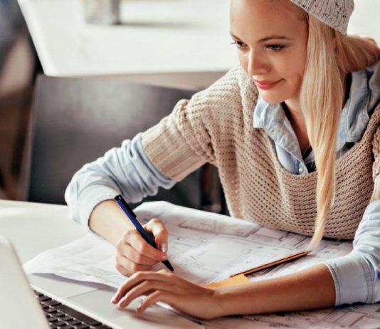 Junge Frau sitzt am Schreibtisch mit Laptop und Stift und Papier.