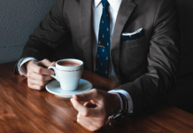 Akademiker aufgepasst – So spannend sind die Karrierechancen in 2017 Mann im Anzug sitzt am Tisch mit einer Tasse Kaffee.