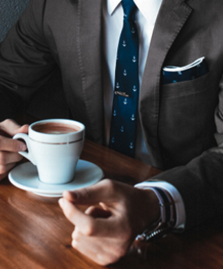 Akademiker aufgepasst – So spannend sind die Karrierechancen in 2017 Mann im Anzug sitzt am Tisch mit einer Tasse Kaffee.