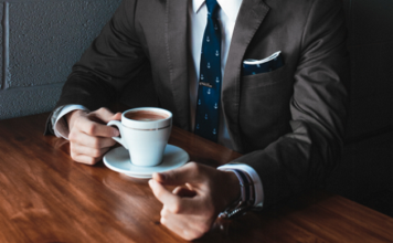 Akademiker aufgepasst – So spannend sind die Karrierechancen in 2017 Mann im Anzug sitzt am Tisch mit einer Tasse Kaffee.
