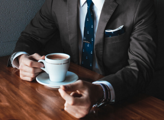 Mann im Anzug sitzt am Tisch mit einer Tasse Kaffee.